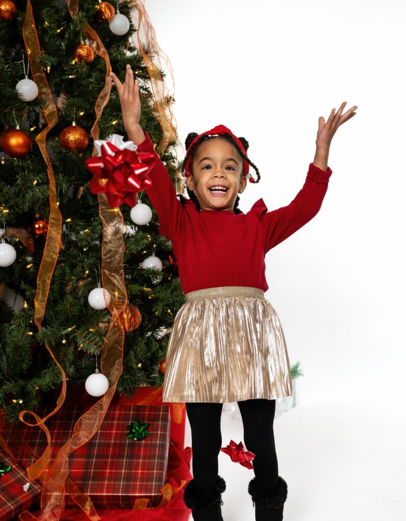 Young girl throwing bows in the air next to a Christmas tree.