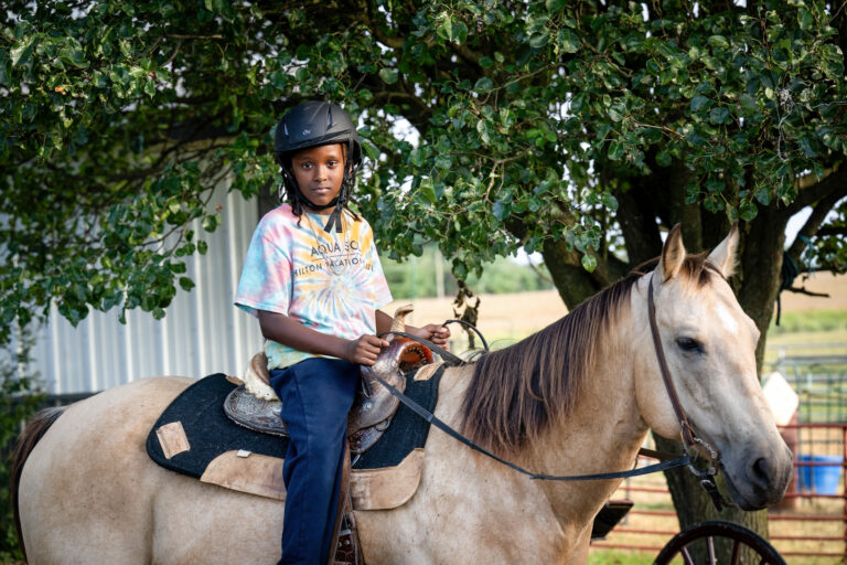 Boy riding a horse on a farm looking and smiling at the camera