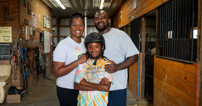 Two adults and a child standing in a barn looking at the camera and smiling