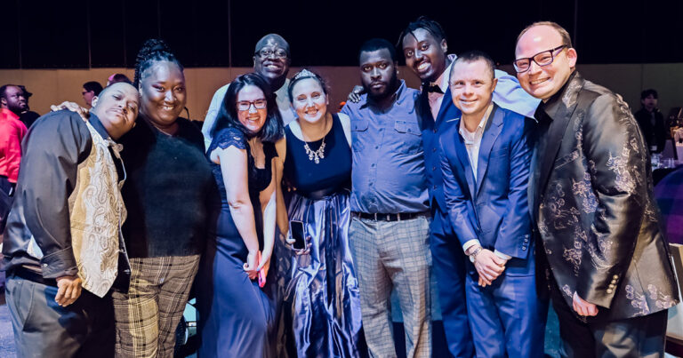 Group of nine people in a dance hall during the Snowflake Ball standing in a group smiling for the camera