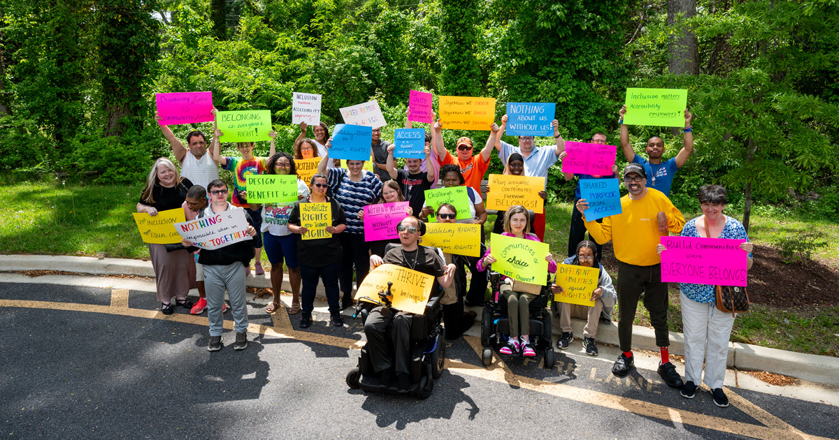 Large group of self-advocates holding up protest signs about the proposed 2027 budget cuts.
