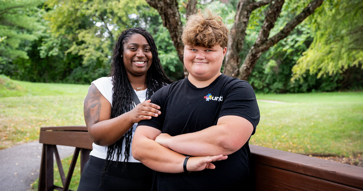 Two people standing on a small bridge in a park smiling for the camera