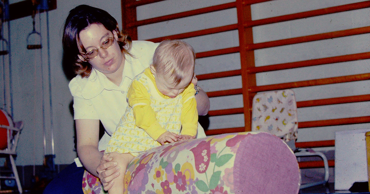 Woman helping a baby balance on a long round pillow