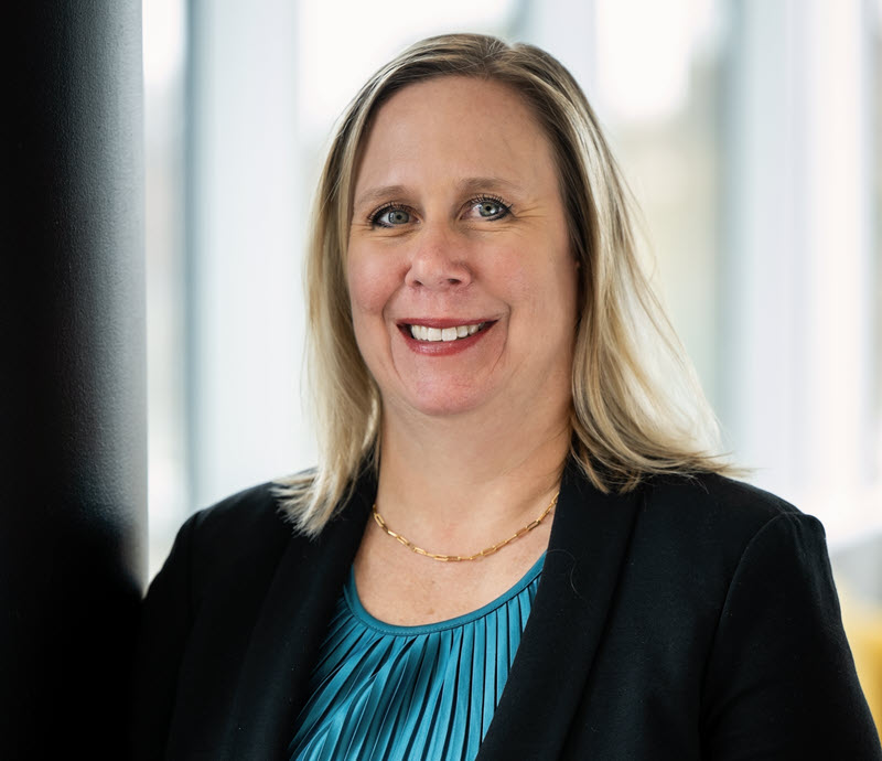 Caroline Slobodzian headshot. She is wearing a black blazer with a teal blouse. She has medium length blonde hair.