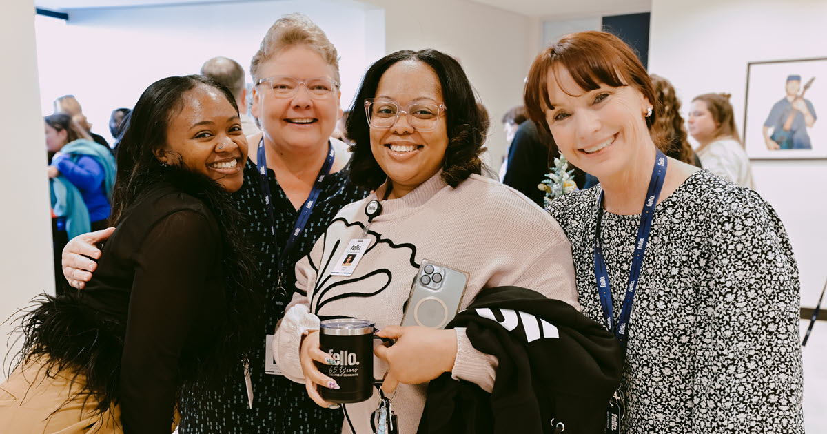 Four people tightly grouped smiling for the camera in a large indoor space