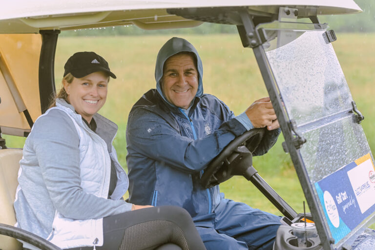 Two people sitting in a golf cart in a rainstorm