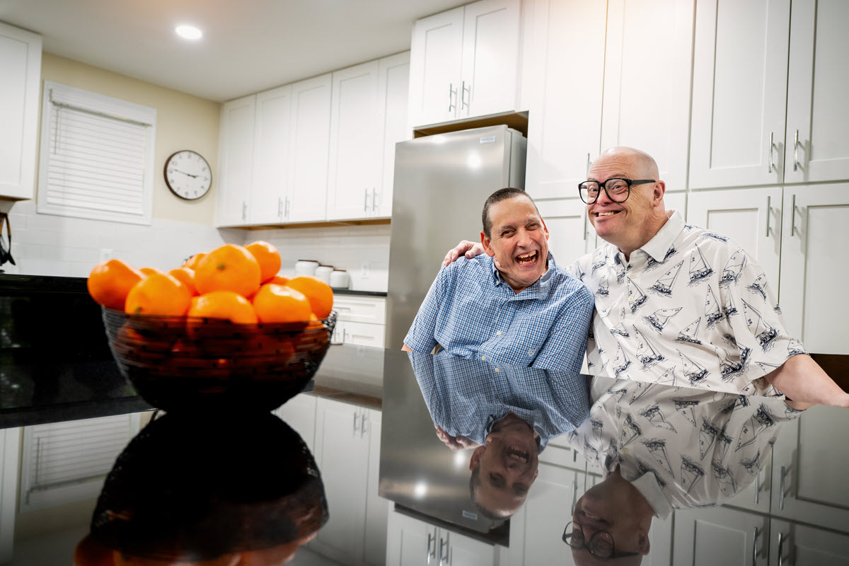 Two people sitting at a kitchen island with a bowl of oranges on the counter