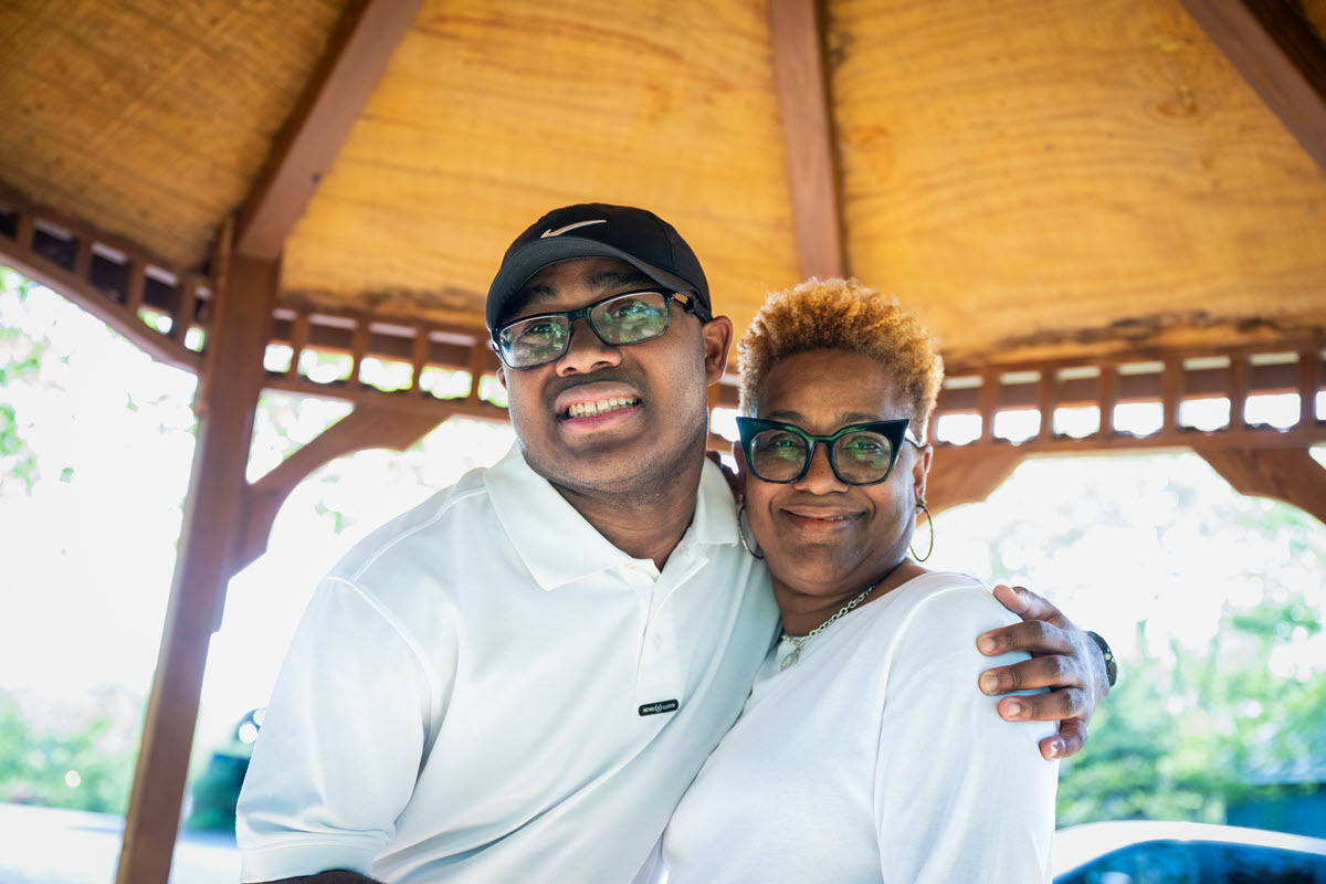 A mom and son hugging and smiling for the camera wearing white shirts and black rimmed glasses