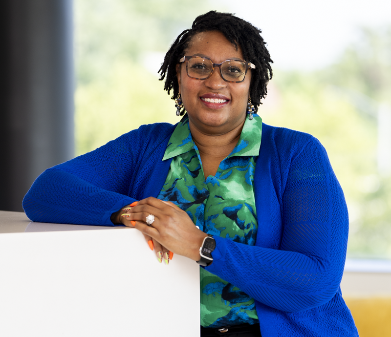 Tyrese Harris - Director of Talent Experience posing for a headshot wearing a blue sweater, blue and green blouse and tortoise shell glasses.