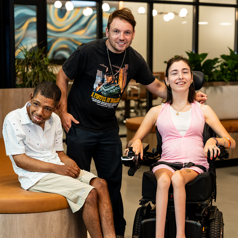 Living Boldly officers posing for a photo. One person is standing the center with one person sitting on a beach and the other in a wheelchair