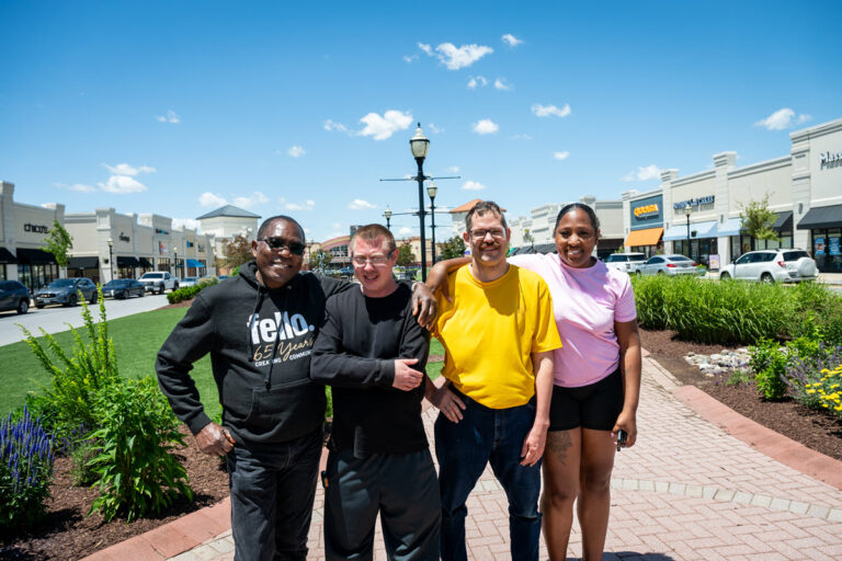4 people standing in a group smiling while standing outside in an outdoor shopping center