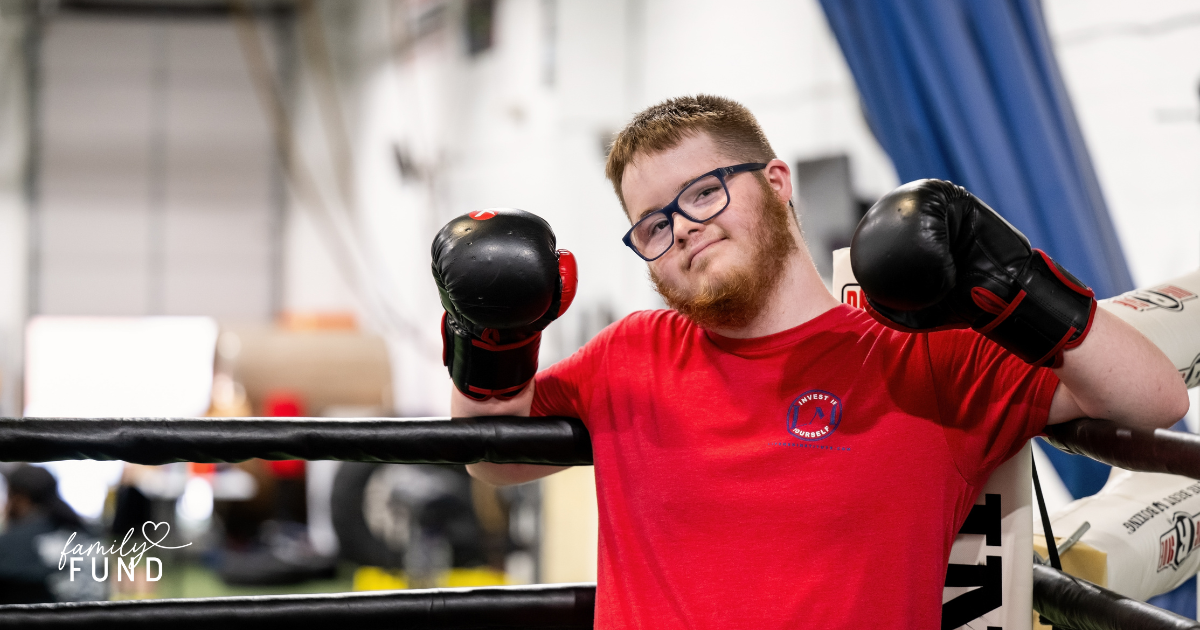 A person wearing a red shirt, boxing gloves and glasses in a boxing ring inside of a gym